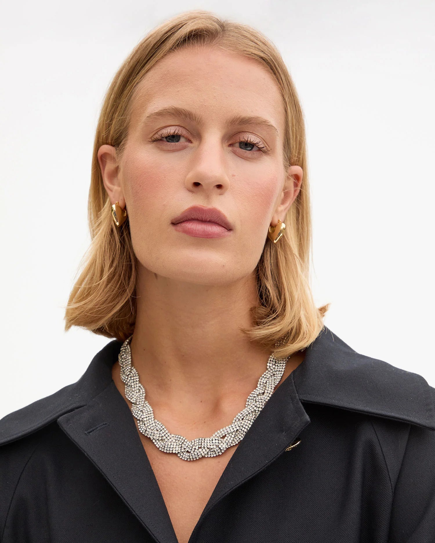 A woman with blonde, shoulder-length hair wears the Clare Vivier Fete Collar, a black collared top, and gold hoop earrings, looking directly at the camera with a neutral expression against a plain background.