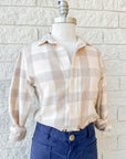 A mannequin wears Frank & Eileen's Silvio Untuckable Shirt in beige and cream plaid, featuring a petite square fit, paired with high-waisted navy pants, standing before a white brick wall.