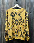 A "C&S Sweats Into the Wild Superwoman" sweater from the I Stole My Boyfriend's Shirt brand is hanging on a wooden hanger against a rustic wooden wall. This stylish piece features an eye-catching yellow and black leopard print, with "Supreme" embroidered in black on the collar for an exclusive touch.