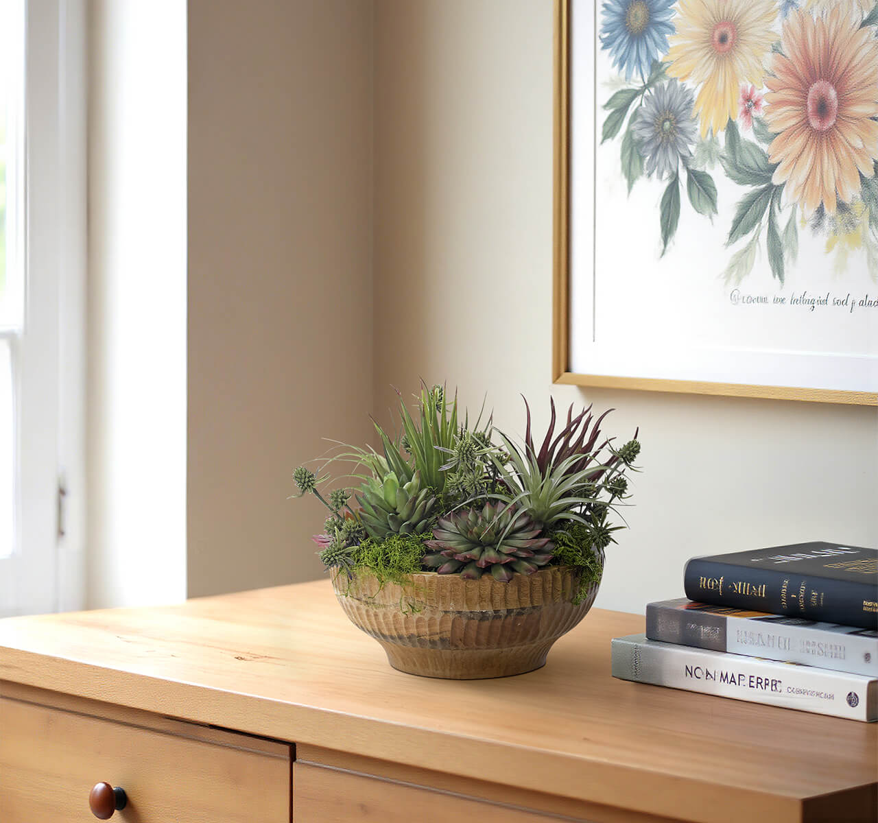 The Succulent Wood Bowl by Natural Decorations Inc. sits on a light wooden dresser near books and floral artwork, creating a charming, maintenance-free display against a cream-colored wall by the window.