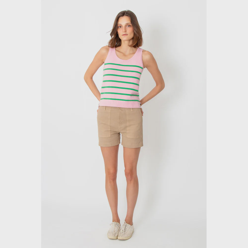 A person stands against a plain background, wearing a pink tank top with green stripes, The City Short by Kule made in Italy from cotton, and white sneakers. Their hands are on their hips.