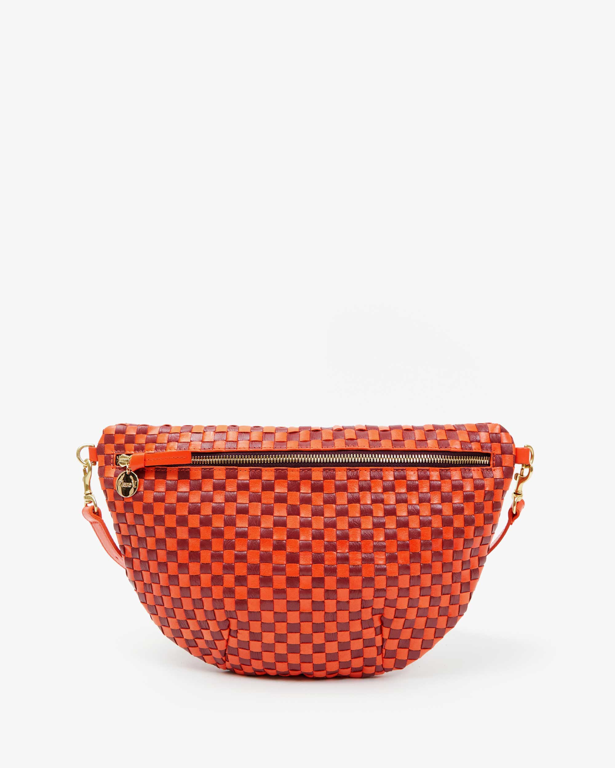 The Grande Fanny Woven Checker by Clare Vivier is a woven crossbody bag with a red and black checkerboard pattern on a white background, featuring top zipper, adjustable straps, and gold-toned side hardware for hands-free use.