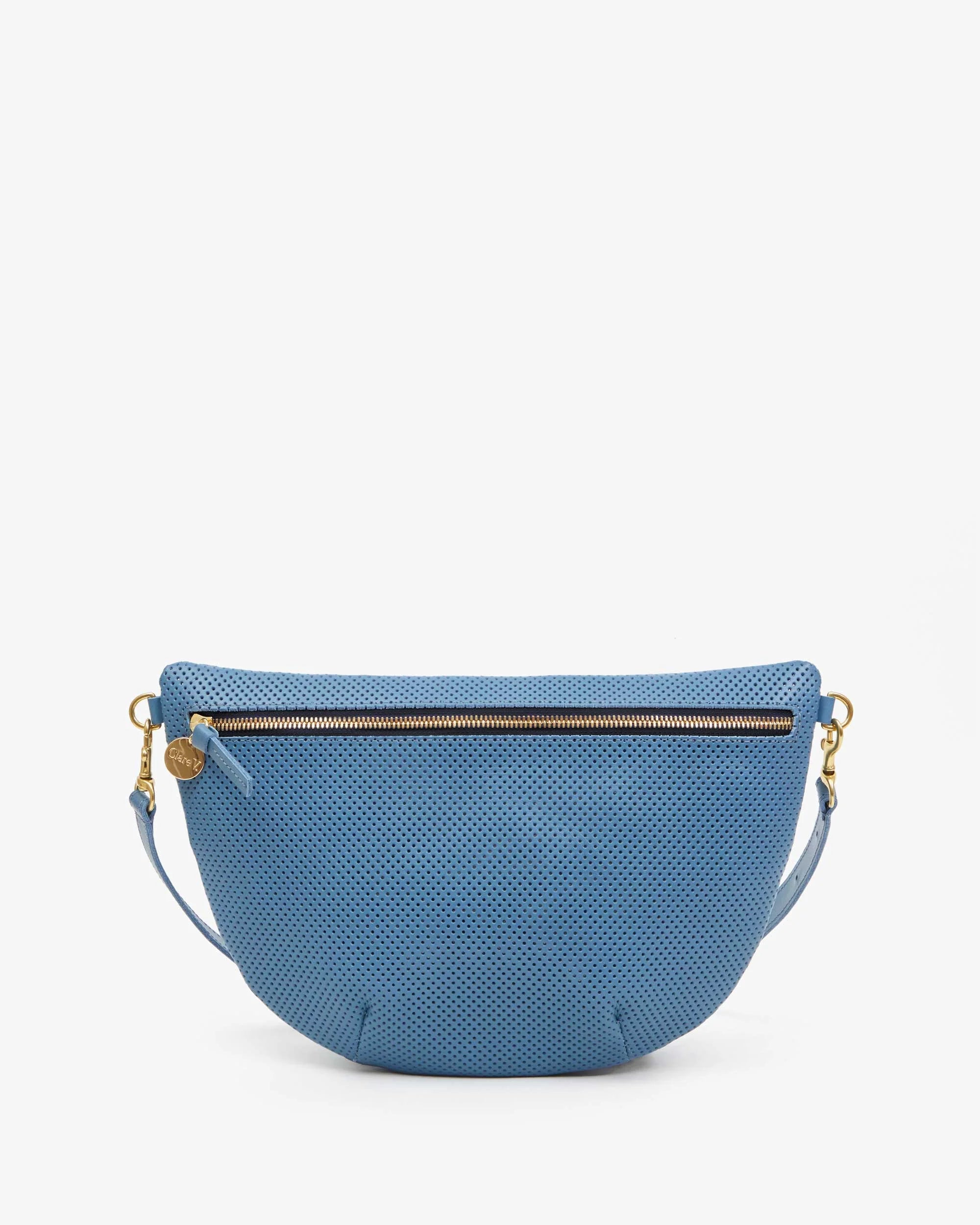 The Clare Vivier Grande Fanny Perf is a blue semi-circular crossbody bag with a textured surface, featuring a top zipper with gold-toned hardware and a round charm. Made in L.A., it includes an adjustable strap for added comfort.