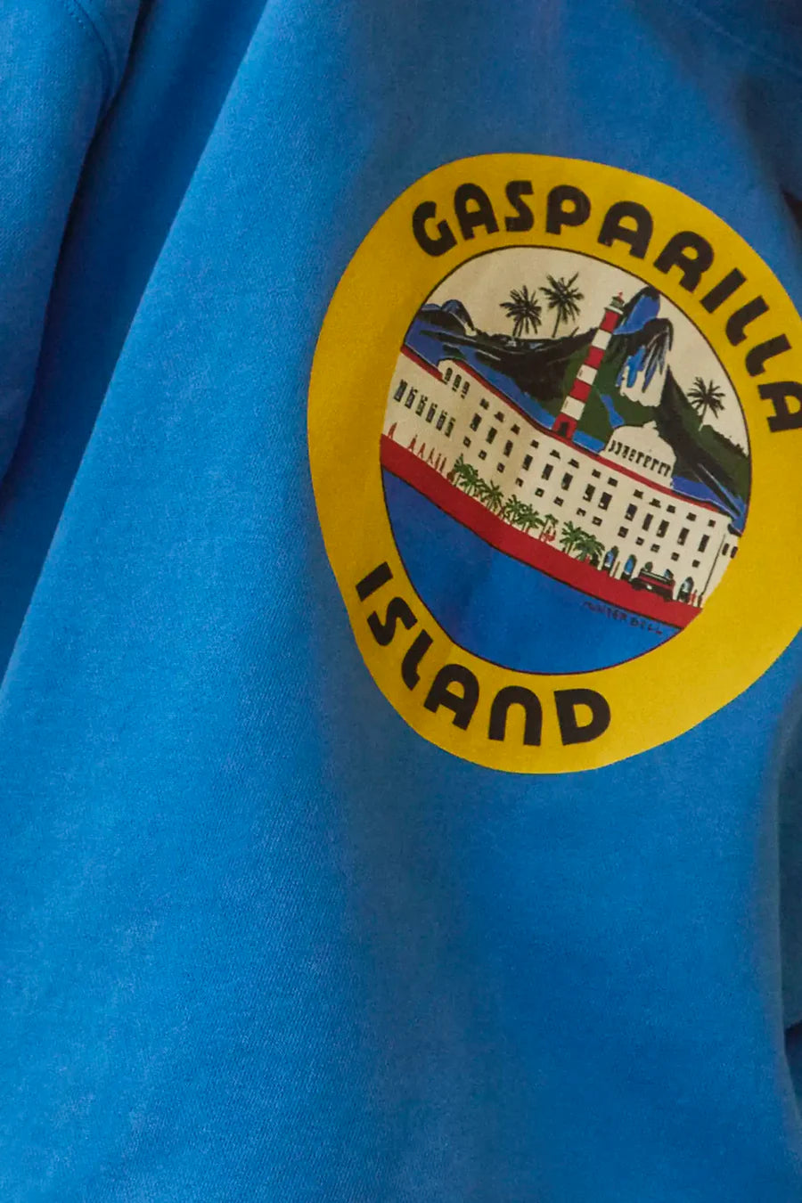 A close-up of Hunter Bell NYC's Graphic Sweatshirt shows a blue, vintage-inspired design. It features "Gasparilla Island" text encircling a coastal scene of a lighthouse, palm trees, and buildings set within a yellow border.