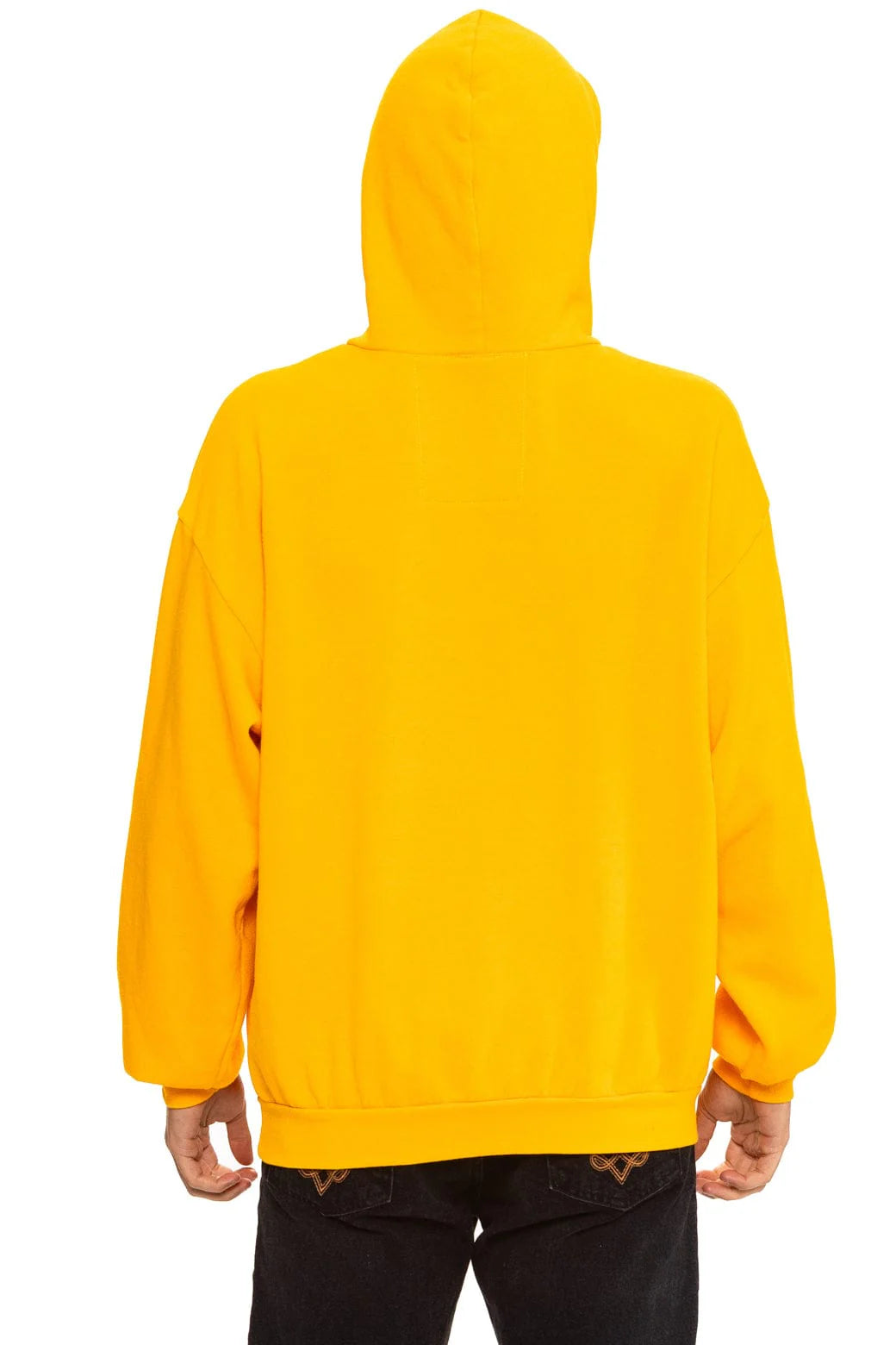 A person is seen from the back wearing Aviator Nation’s logo - pullover hoodie relaxed in bright yellow with the hood up and black jeans, against a plain white background.