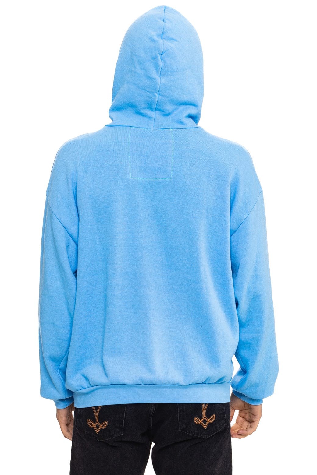 A person is shown from the back wearing the Aviator Nation mountain stitch chevron - pullover hoodie relaxed in bright blue with the hood up, paired with black jeans featuring decorative stitching. The background is plain white.