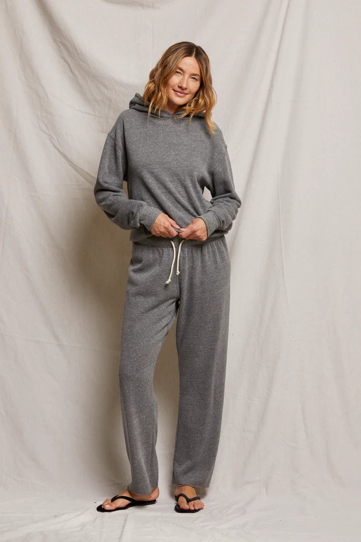 A person in a relaxed pose embodies effortless style in Perfectwhitetee's Collins Straight Sweatpant, paired with a gray hoodie. The cotton fleece set is complemented by black flip-flops, all against a neutral, draped fabric backdrop.