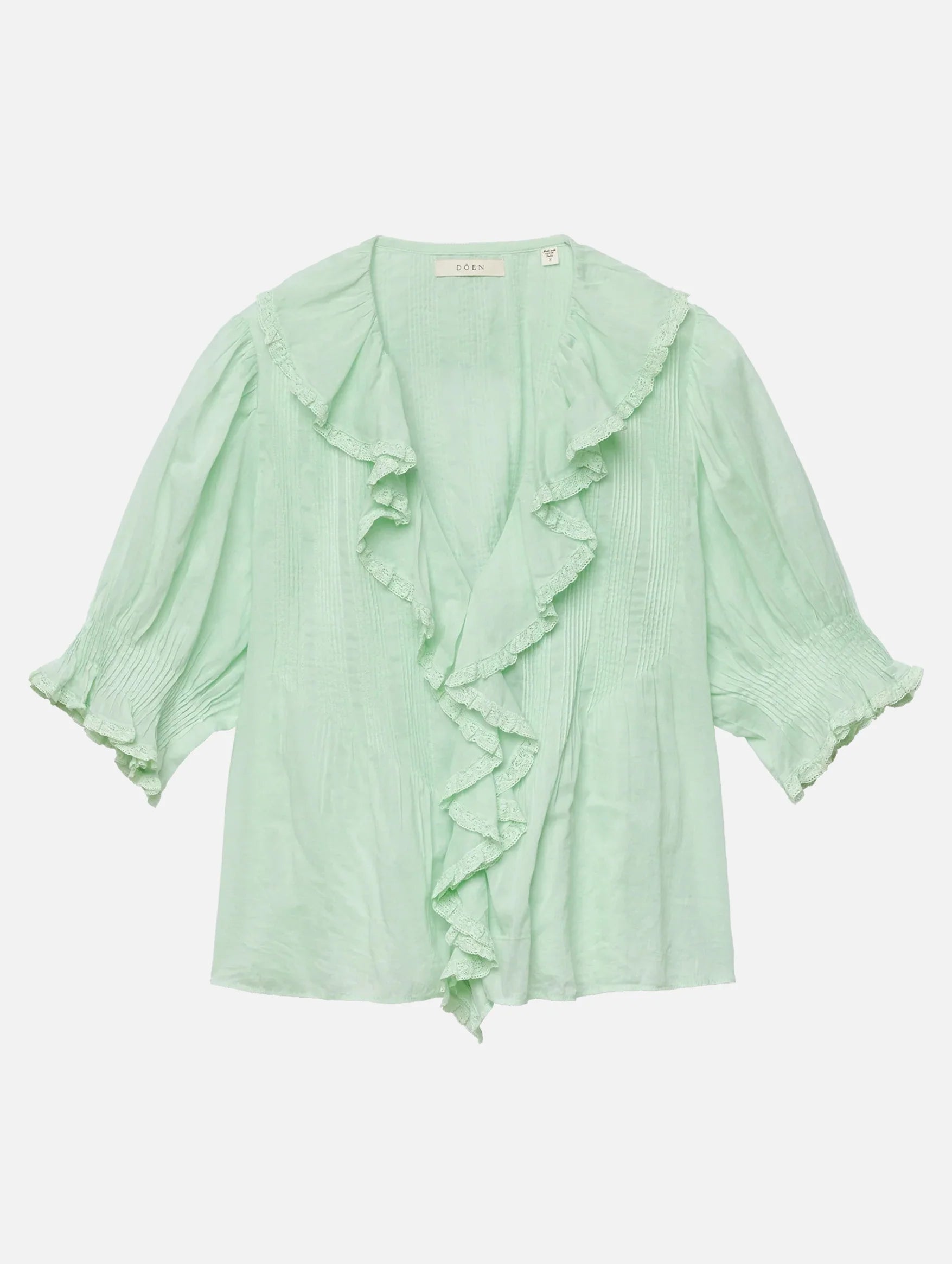 The DOEN Henri Top is a light green organic cotton blouse with short puff sleeves, ruffled neckline and front, gathered sleeve details, and a flowy lightweight fabric for a feminine Edwardian-inspired look.