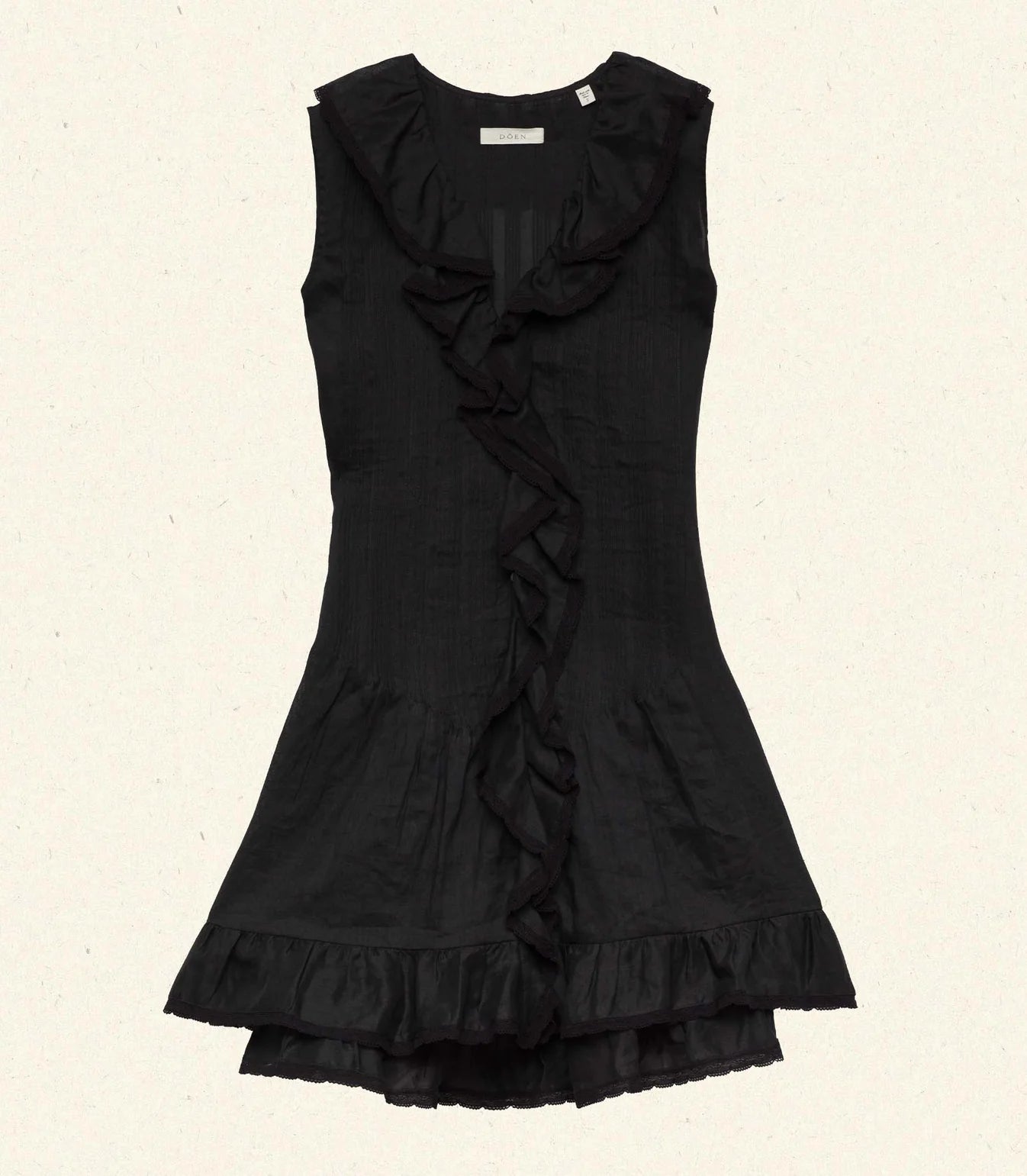 The DOEN Henrietta Dress is a sleeveless black ramie mini dress with lace-trimmed ruffles at the neckline, front, and hem. Featuring a fitted bodice and flared skirt, it’s shown laid flat on a light backdrop.