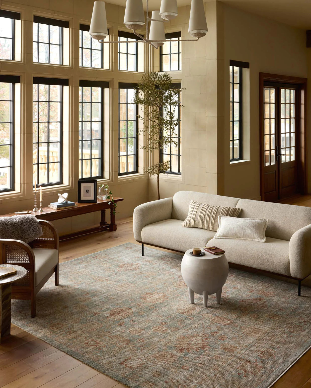 Elegant living room with large windows, cream sofas, a Loloi Rugs Aqua/Terracotta rug, and wooden floors in Arizona-style bungalow, evoking a warm and welcoming ambiance.