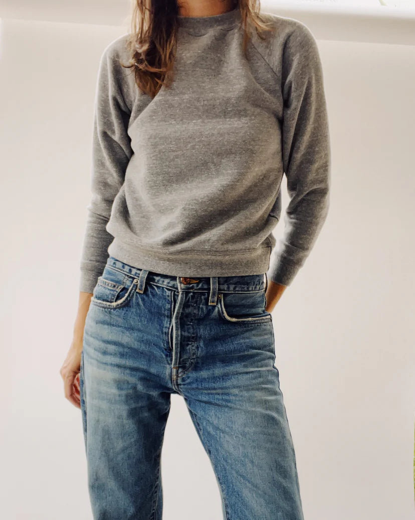 A person wearing The Sweatshirt by Hey Gang and blue jeans stands against a plain white background, with their right hand in their pocket.