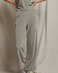 A person stands against a beige backdrop wearing a light gray t-shirt and the Holly Velour Wide Leg Sweatpant from Perfectwhitetee, with their hands tucked into the pockets and metallic sneakers on their feet.