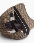 A close-up of the Rag & Bone harlow baseball cap showcases its brown plaid pattern, black adjustable strap with a metal clasp, and intricate stitching along the inner brim.