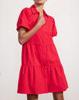 A person wears the bright red BROCHU WALKER HAVANA MINI DRESS, a short-sleeve, button-down mini dress with a tiered skirt and collar, standing against a plain light background.