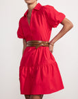 A woman wearing the BROCHU WALKER HAVANA MINI DRESS in bright red, featuring puff sleeves and a tiered skirt with a brown wrap belt, poses against a plain white background. Her head is slightly tilted and her face is partially cropped.