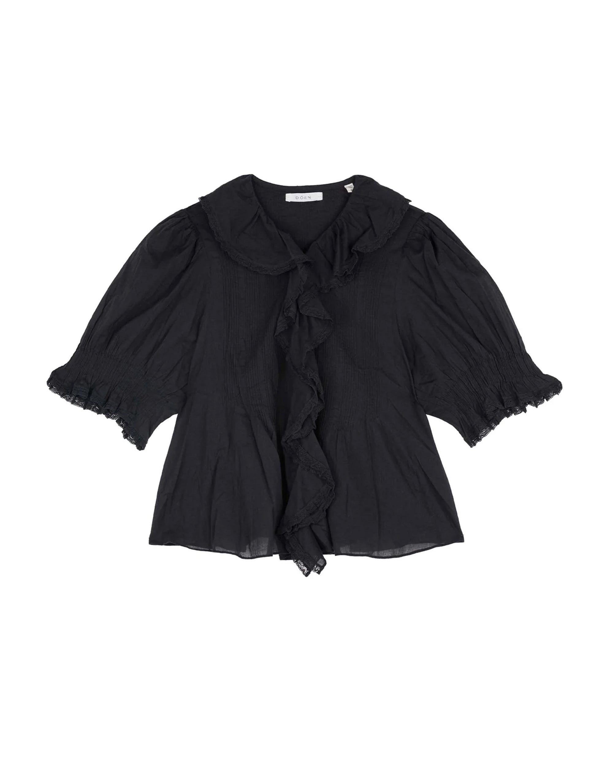 The Henri Top by DOEN is a black, short-sleeved, Edwardian-inspired blouse featuring puffed sleeves, a ruffled lace-trimmed collar and front, and elastic smocked cuffs. Made from lightweight organic cotton voile that's slightly sheer.