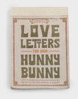 The 150 Love Letters for Your Hunny Bunny notepad by Sugarboo Designs has a beige cover with bold green and orange title text. It features perforated pages, a decorative border, and a charming "Sugarboo & Co." banner on top for sharing cherished notes.