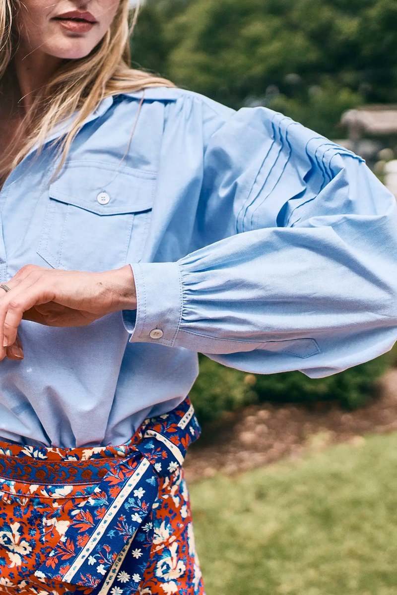 Evangeline blue puff-sleeve oxford shirt by Hunter Bell NYC styled with a patterned red skirt outdoors.
