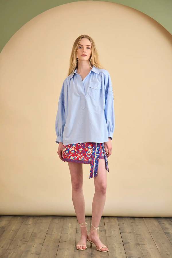 Evangeline shirt by Hunter Bell NYC styled with a floral wrap skirt against a neutral beige background.