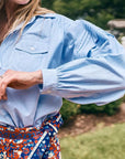 Evangeline blue puff-sleeve oxford shirt by Hunter Bell NYC styled with a patterned red skirt outdoors.