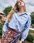 Evangeline blue oxford shirt and floral skirt by Hunter Bell NYC worn outdoors in a sunlit, relaxed lifestyle setting.