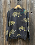 A "C&S Sweats Into the Wild Superwoman" sweatshirt from I Stole My Boyfriend's Shirt, featuring a silk screen print of yellow and black tigers, is hanging on a wooden wall. The teal "Supreme" logo on the upper left side near the shoulder adds a striking contrast to this bold design.