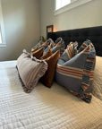 A neatly made bed with a dark upholstered headboard features four decorative pillows: two brown velvet and two Rennah Collective Foxy Blue Striped Ruffle Pillows (22x22), all arranged on a crisp white quilted bedspread.