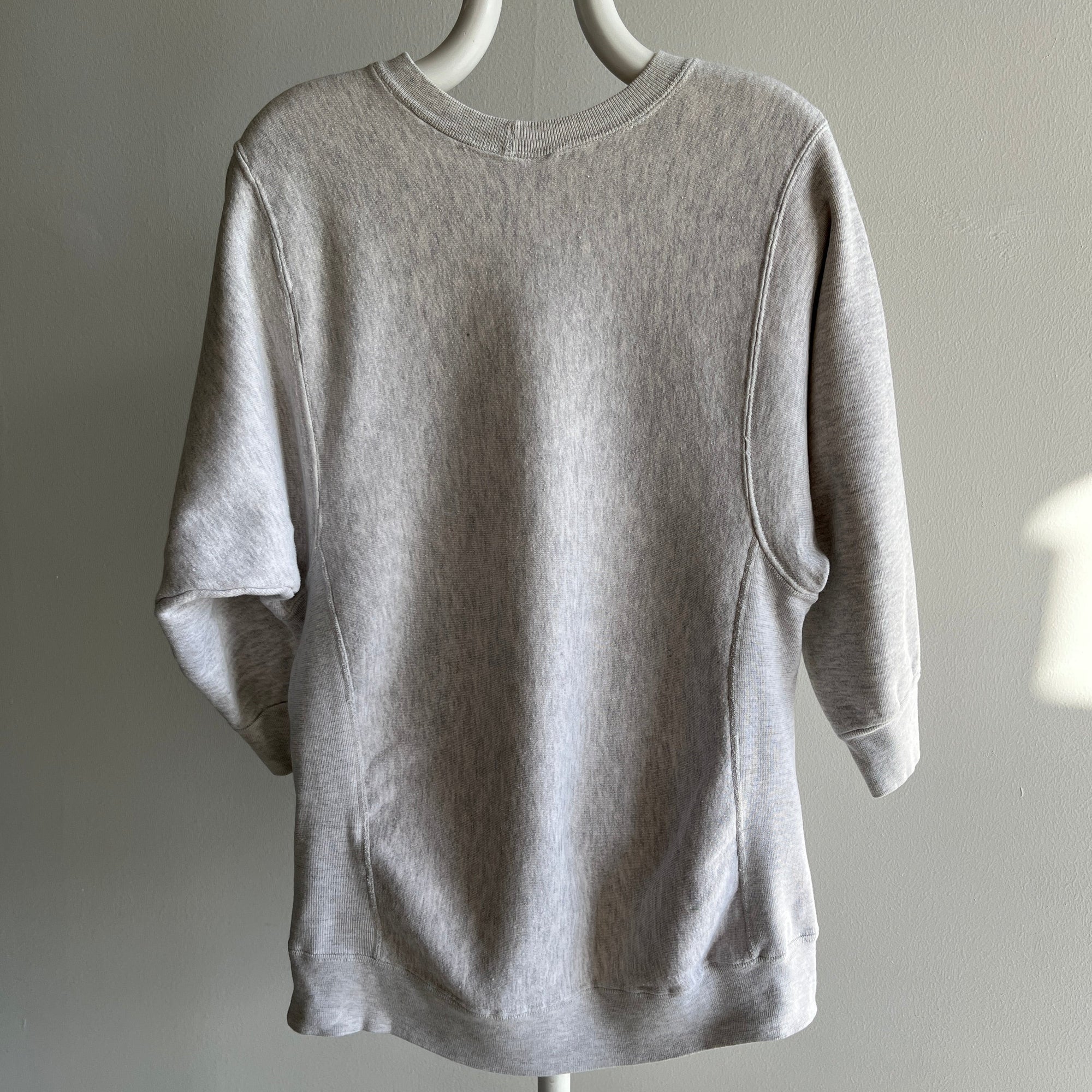 The 80s NYU Law School Half Sleeve Sweatshirt by Red Vintage Co. is showcased on a hanger against a plain wall. Viewed from the back, its soft and relaxed design with long sleeves embodies that perfect vintage clothing vibe.