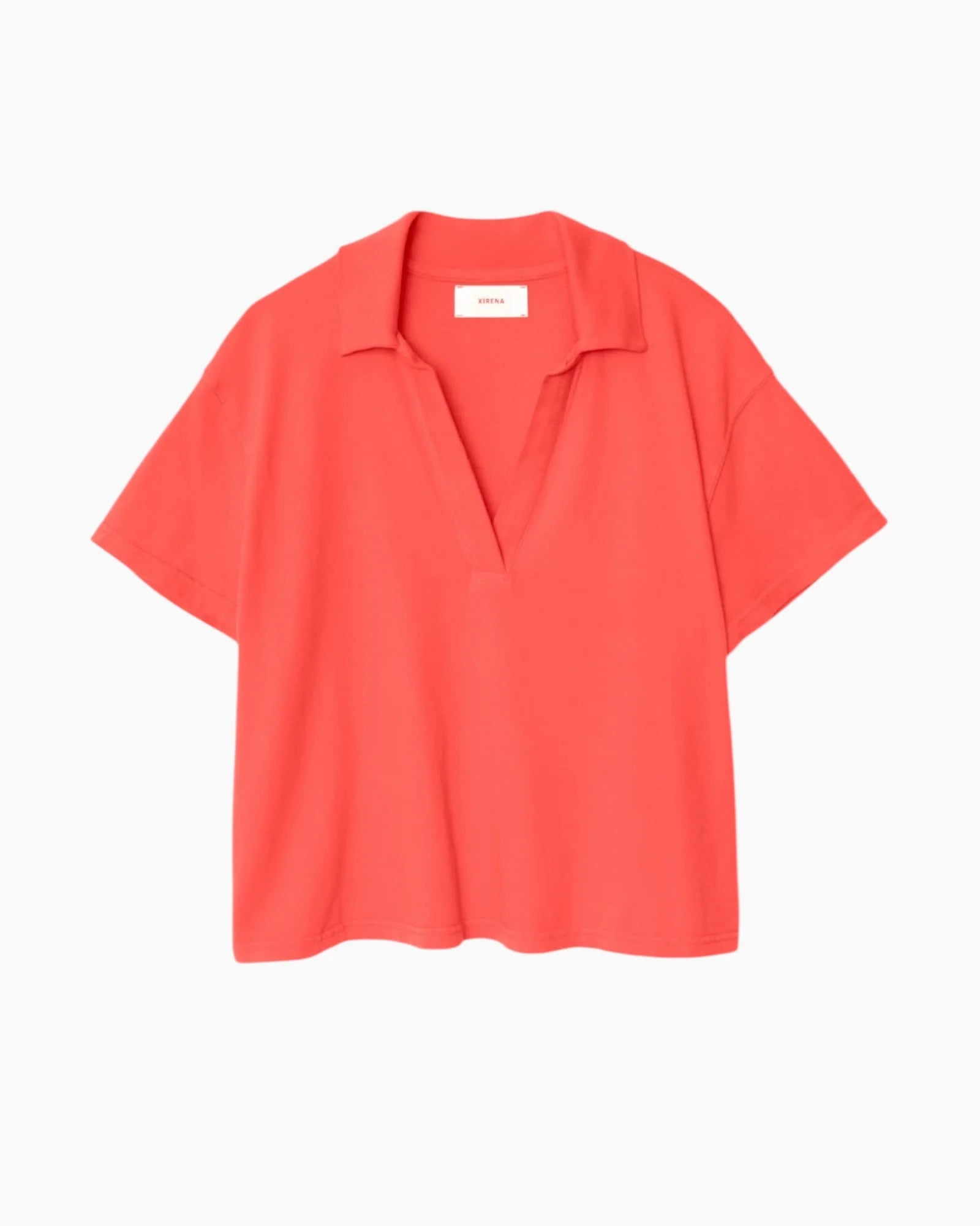 The Spencer Tee by Xirena is a coral red, short-sleeved cotton polo with an open collar and relaxed fit, no buttons, made in Los Angeles and shown against a plain white background.