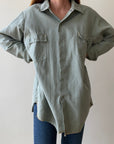 A person wearing the Red Vintage Co. 1950s Sage Canvas Workshirt—a loose, heavyweight button-up with two chest pockets—and blue jeans stands against a plain light background, hands on hips.