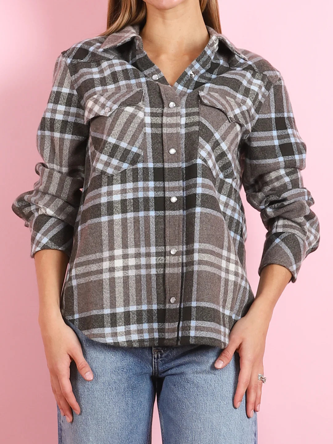 Someone wearing the BCS Group Lumber L/S Shirt—a gray, black, and white plaid 100% cashmere button-up with rolled-up sleeves—and light blue jeans stands against a pink background.