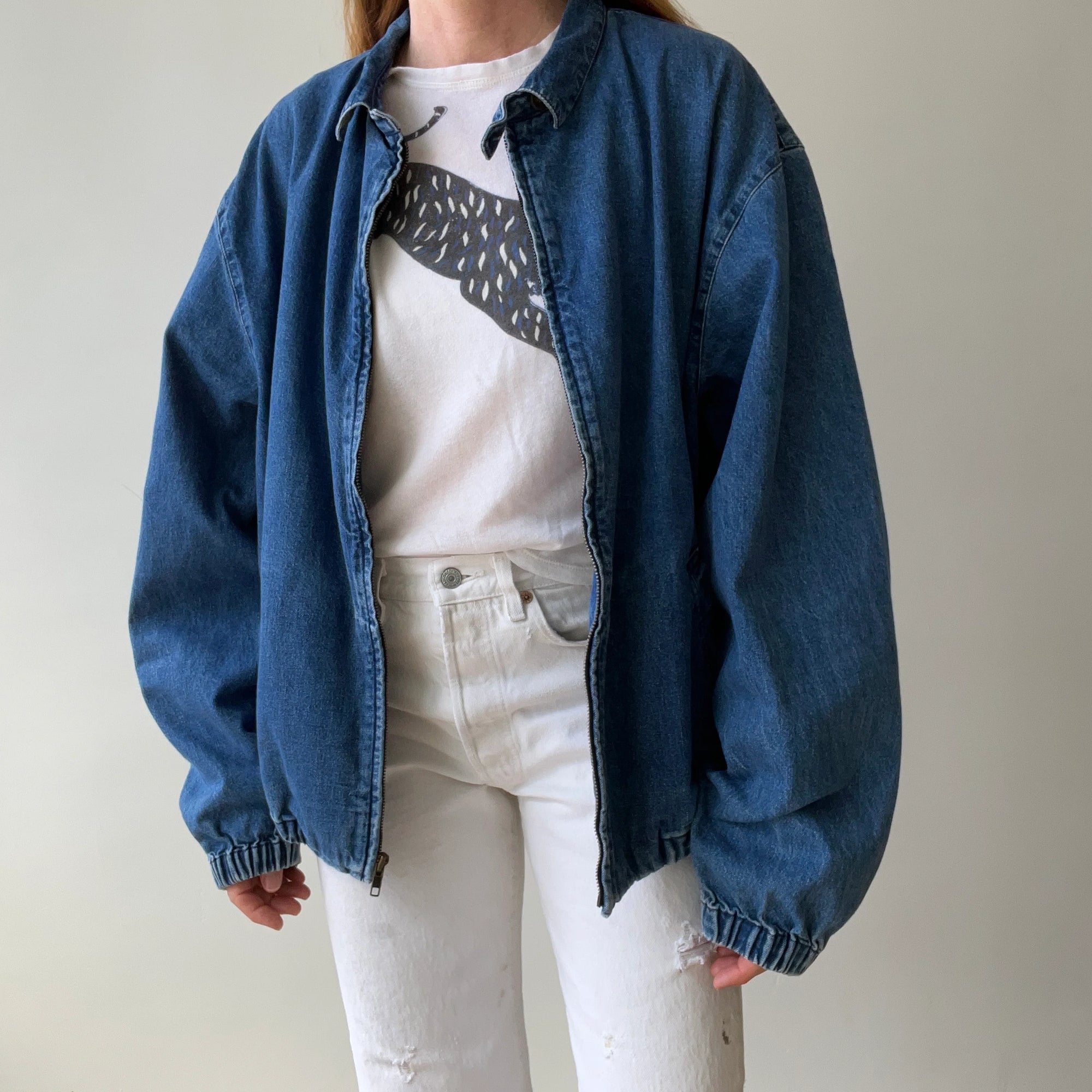 A person models the Red Vintage Co. 90s RL Denim Dad Jacket with plaid details, layered over a white graphic tee and high-waisted white jeans, standing against a plain light background. Their head is not shown.