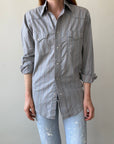 A person models the 80s Wrangler Button Up from Red Vintage Co.—a sun faded, pearl snap shirt with thin vertical stripes—paired with light blue distressed jeans, standing against a plain light background. Face not visible.