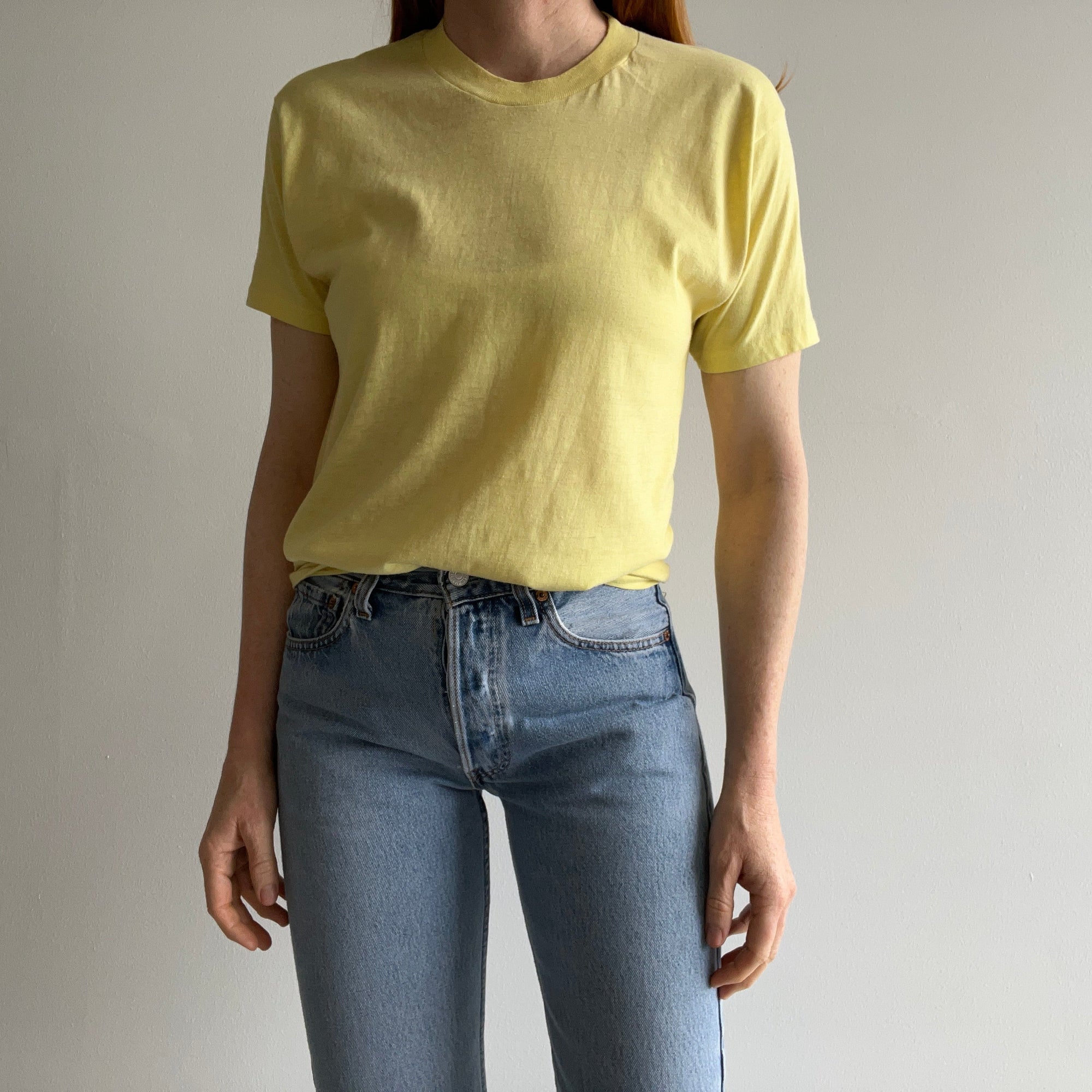 A person stands against a plain background, wearing an 80s Stroh St. Paul MN Beer Tee by Red Vintage Co., paired with blue jeans that evoke Midwestern charm. Their hands are relaxed by their sides.