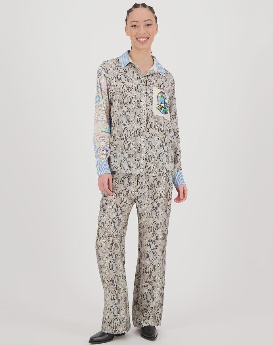A person smiles, wearing the Me369 Bailey Track Pant with a matching button-up shirt featuring a gray abstract pattern, blue cuffs and collar, paired with black shoes, all set against a plain white background.