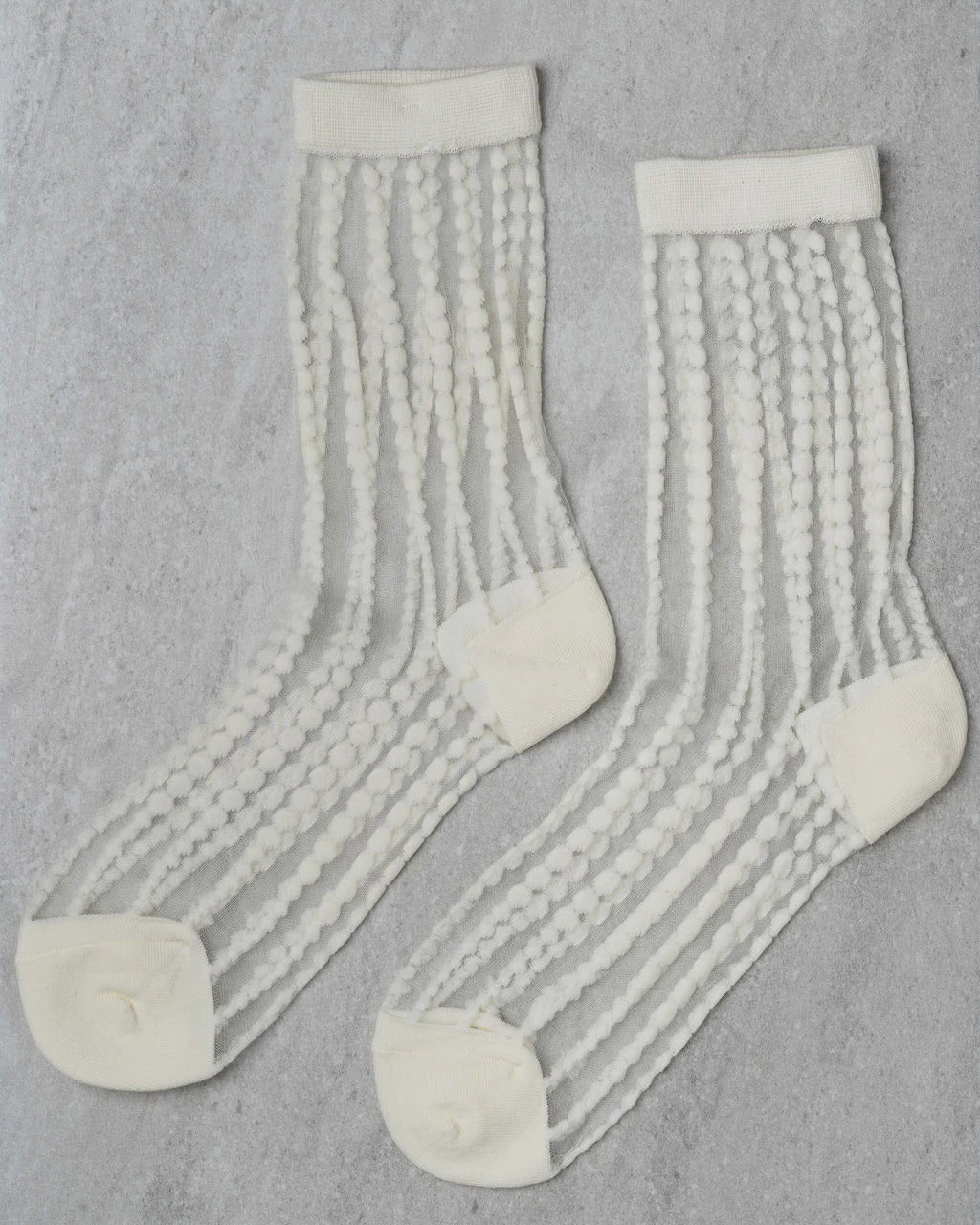 The Unified Sheer Bubble Sock is a white crew sock with opaque polka dot stripes, shown laid flat on a light gray textured surface.