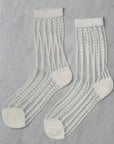 The Unified Sheer Bubble Sock is a white crew sock with opaque polka dot stripes, shown laid flat on a light gray textured surface.