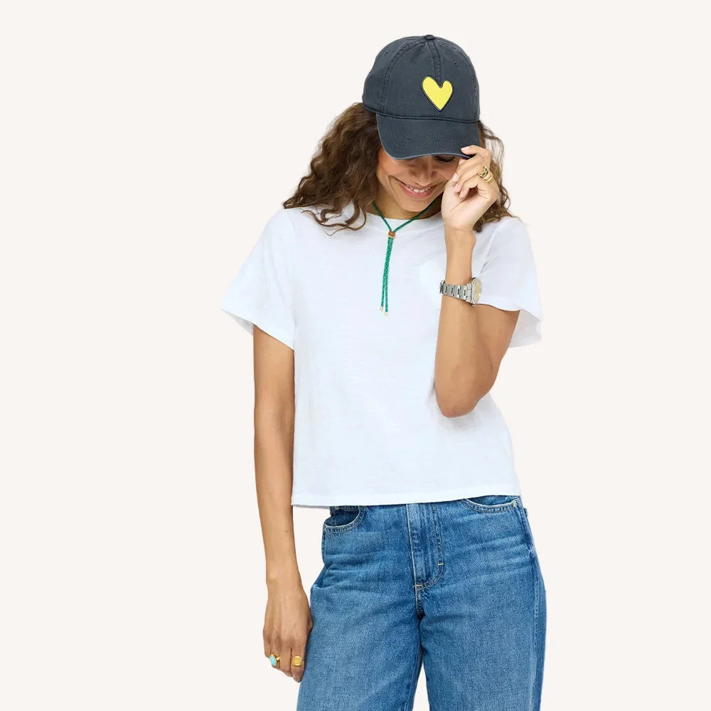 KR Imperfect Heart Hat by Kerri Rosenthal with heart patch, worn casually with jeans and a white tee, smiling.