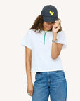 KR Imperfect Heart Hat by Kerri Rosenthal with heart patch, worn casually with jeans and a white tee, smiling.