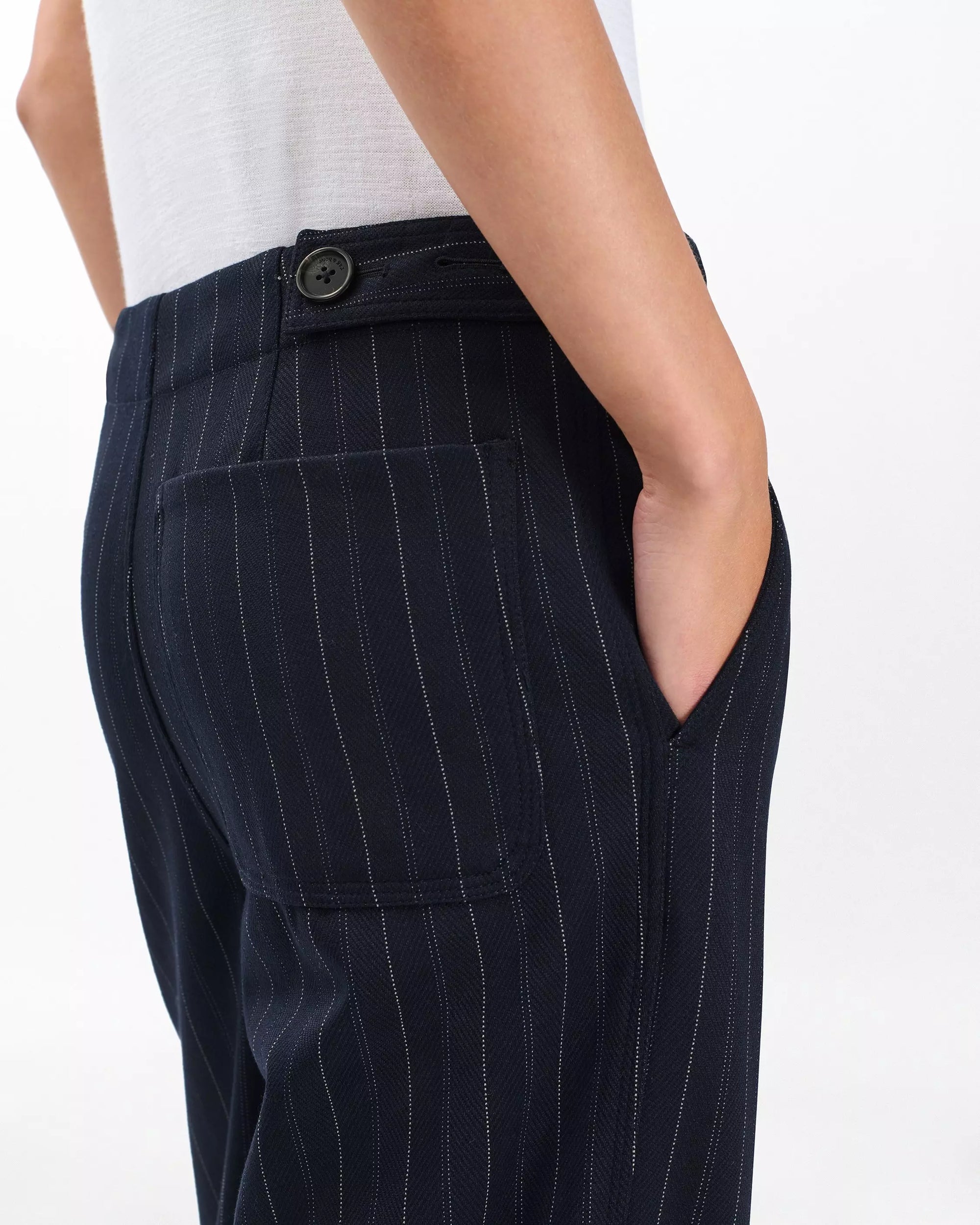 A person wearing Rag & Bone irina ponte tailored pants, shown waist down with one hand in a side pocket, displaying the dark navy wide-leg design with pinstripes and back pocket against a plain white background.