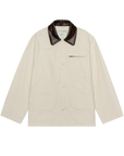 The Great Inc. Barn Jacket in cream cotton canvas features a dark brown leather collar, front buttons, utility pockets—including a zippered chest pocket—and two large front pockets, shown laid flat on a white background.