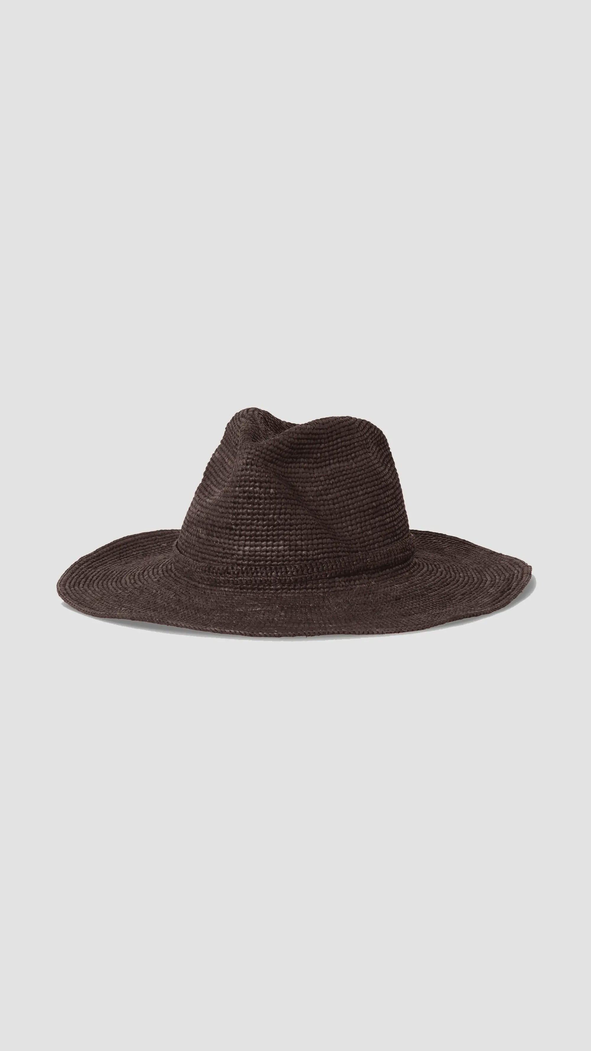 The Sacha Chocolate hat by Janessa Leone is a wide-brimmed, dark brown western fedora with a pinched crown, hand-crocheted from Madagascar straw, shown against a plain light gray background.