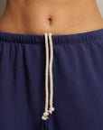 A close-up view of a person's midsection showcases the French Terry Easy Sweatpant by Perfectwhitetee, featuring navy blue fabric made from French terry cotton. The white drawstrings hang loosely at the waistband, emphasizing elevated comfort wear.