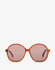 Front view of stylish Jane Sunglasses by Clare Vivier, featuring oversized oval lenses with a brown tint and a slim, glossy orange frame. Crafted with recycled materials, these sunglasses offer UVA/UVB protection. The plain white background emphasizes the sleek design and modern look.