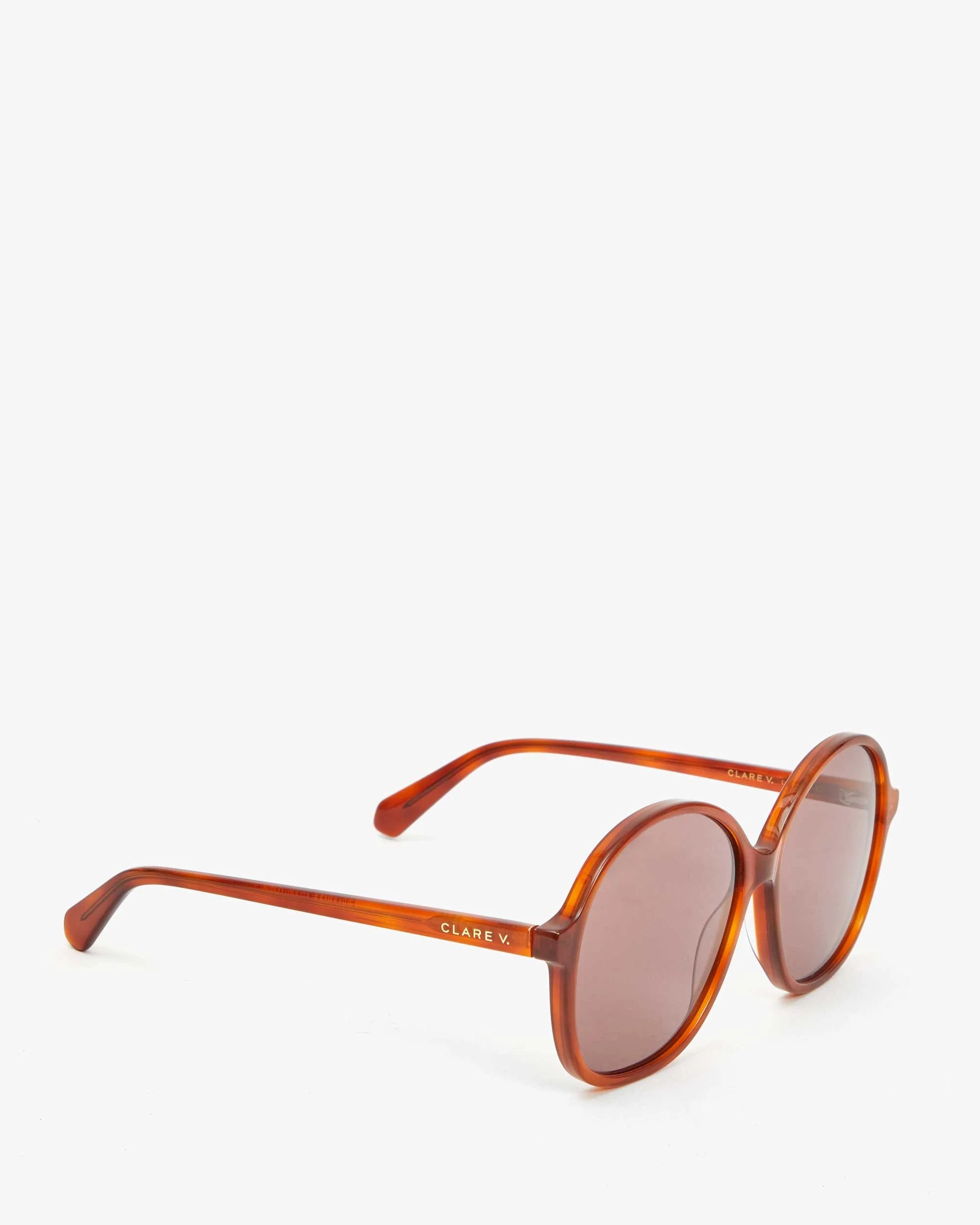 A pair of Jane Sunglasses from Clare Vivier, featuring round tortoiseshell frames with brown lenses that offer UVA/UVB protection. The temple is adorned with "Clare V." in white text and crafted from recycled material. The glasses are displayed on a white background.