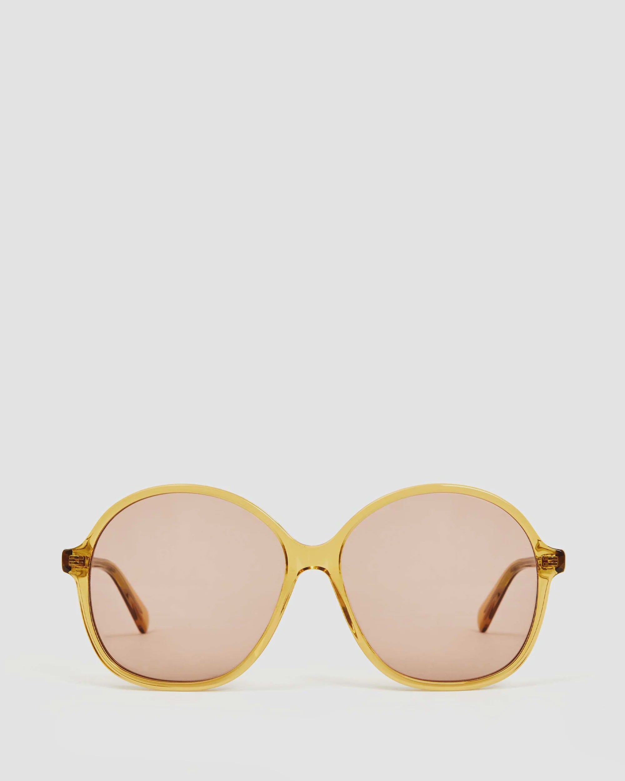 Introducing the Jane Sunglasses by Clare Vivier: A pair of stylish sunglasses with rounded frames crafted from bio acetate in a light amber hue. The lenses are tinted brown, offering full UVA/UVB protection. The matching amber-colored arms complete the look, all set against a light gray background.