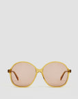 Introducing the Jane Sunglasses by Clare Vivier: A pair of stylish sunglasses with rounded frames crafted from bio acetate in a light amber hue. The lenses are tinted brown, offering full UVA/UVB protection. The matching amber-colored arms complete the look, all set against a light gray background.