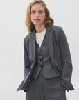 A woman with wavy blonde hair wears the Rag & Bone jennifer striped combo blazer over a white top as a sharp suit, standing confidently against a light background.