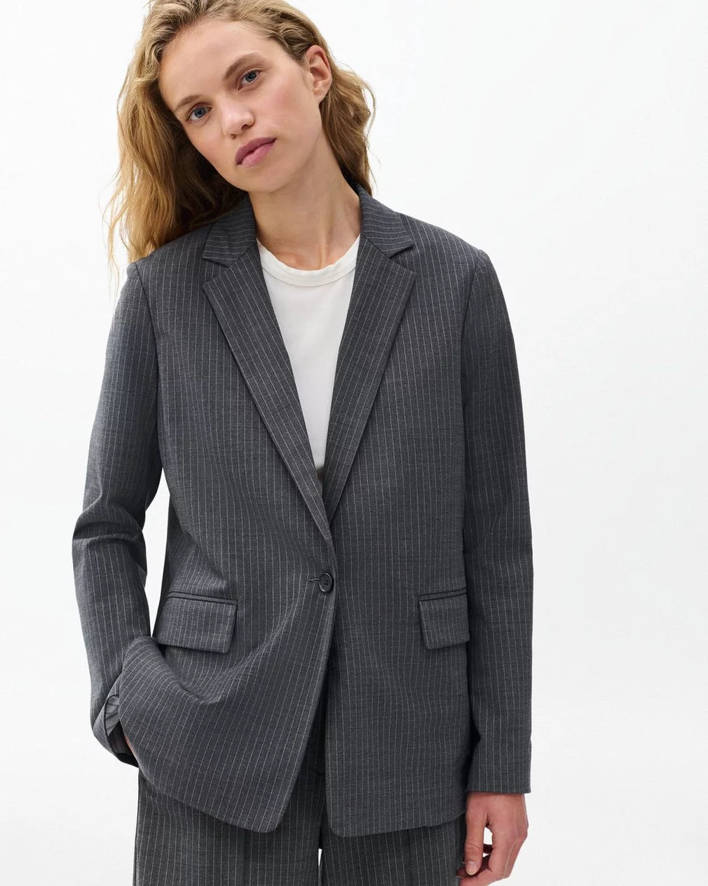 A person with long blonde hair wears the Rag & Bone jennifer striped combo blazer over a white shirt, standing against a plain white background with one hand in their pocket.