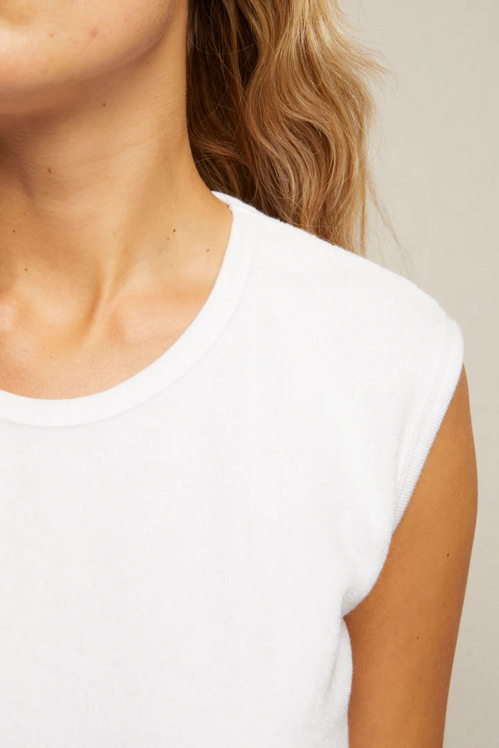 Close-up of a person's neck, shoulder, and part of their face. They are wearing the Perfectwhitetee ELLIE terry banded tank featuring a white ruched waistline. Their light brown wavy hair is partially visible against a neutral, blurred background.